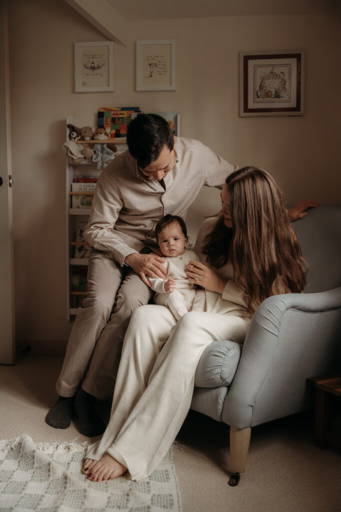 Four month old baby sat in mother's lap whilst Dad looks on doing it at home photo shoot