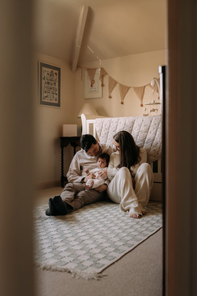Photo of parents sat on a nursery floor at home during a photo shoot in Hampshire with therefore month old baby