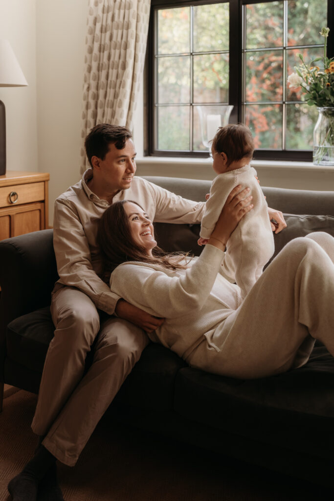 Four month old baby being held up by Mum as she lays into the dad's lap during a photo shoot at Home in Hampshire