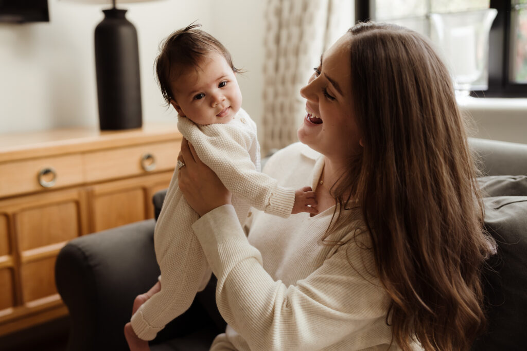 Photo of Mum smiling as she lifts up her four month old baby during an at home family photo shoot in Hampshire
