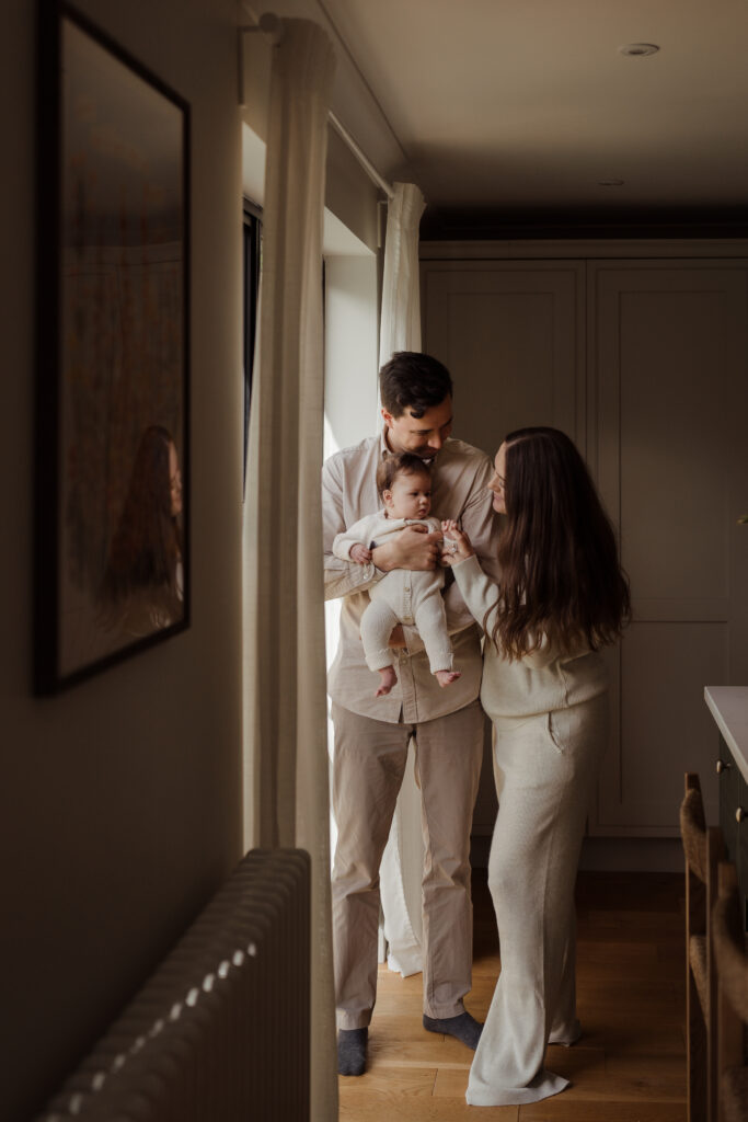 Photo of four month old in her dad's arms during an at home shoot they are stood by the window in the kitchen at the Hampshire Home
