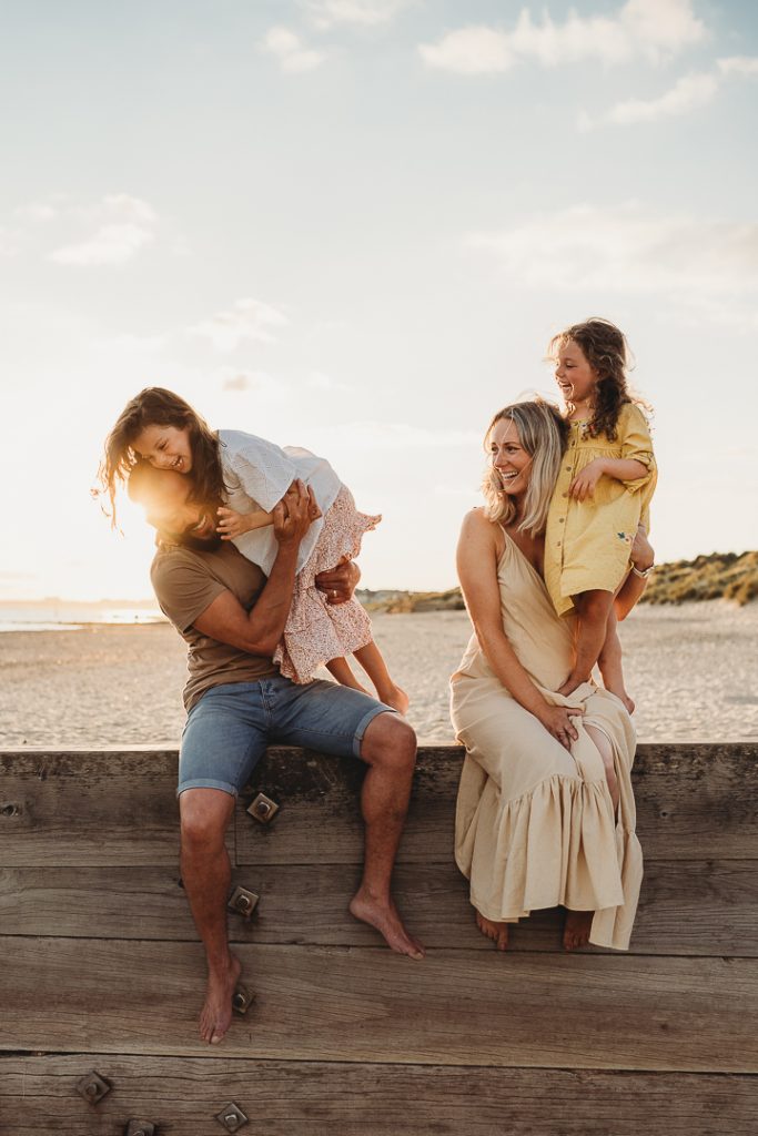 Family sitting on a groin on the beach laughing with su flare poking out from dads head. 