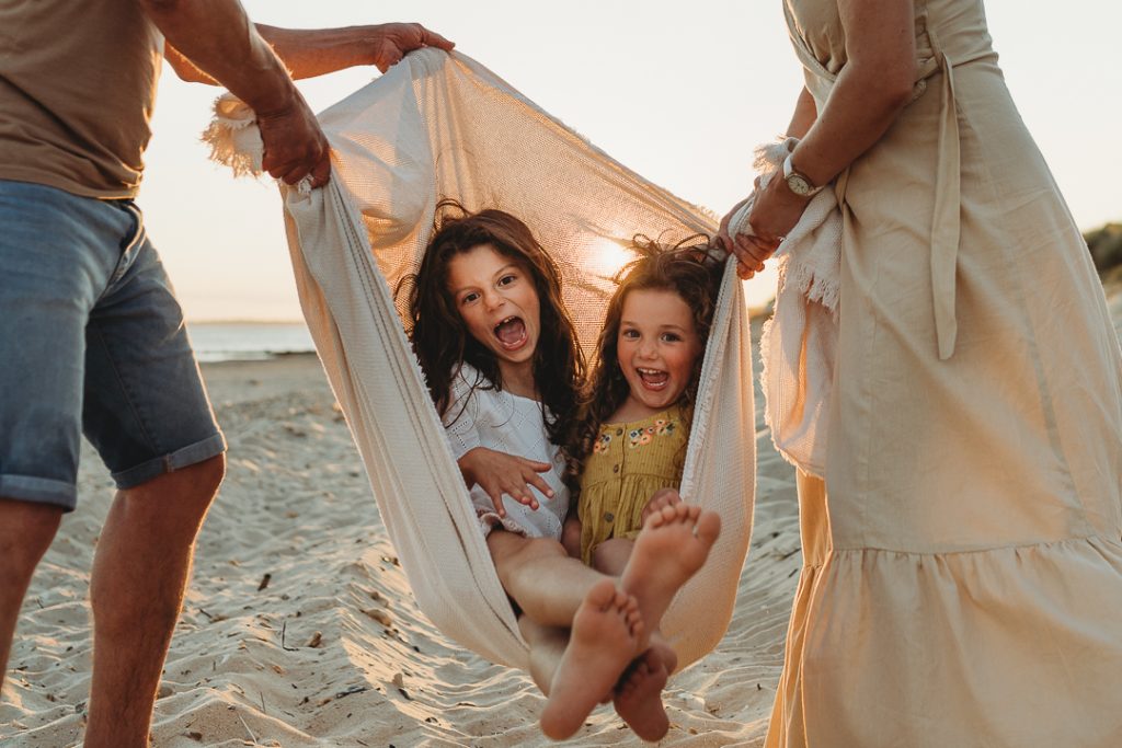 laughing girls being swung in the blanket on the beach with their parents either side at sunset