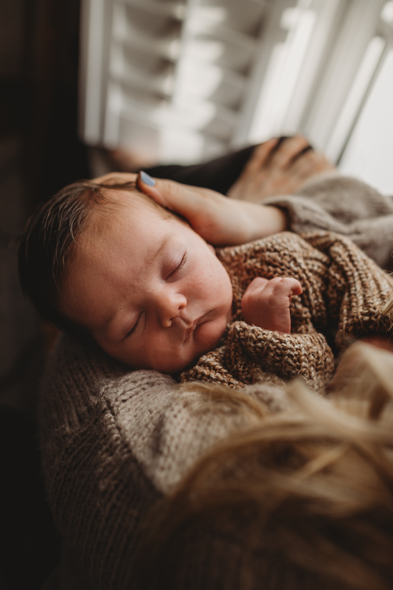 NEWBORN baby in window light wearing knitted cardigan with mother
