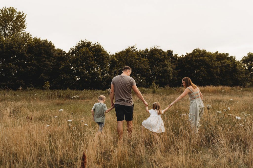 A family of four walking away from the camera in a field of long grass during a sunset photo shoot