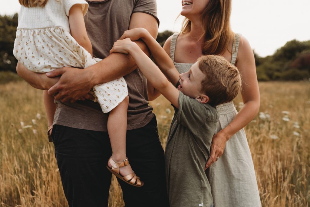 Close-up photographs of a family where the boy is reaching up to his dad and touching him on the arm during a sunset family photo shoot