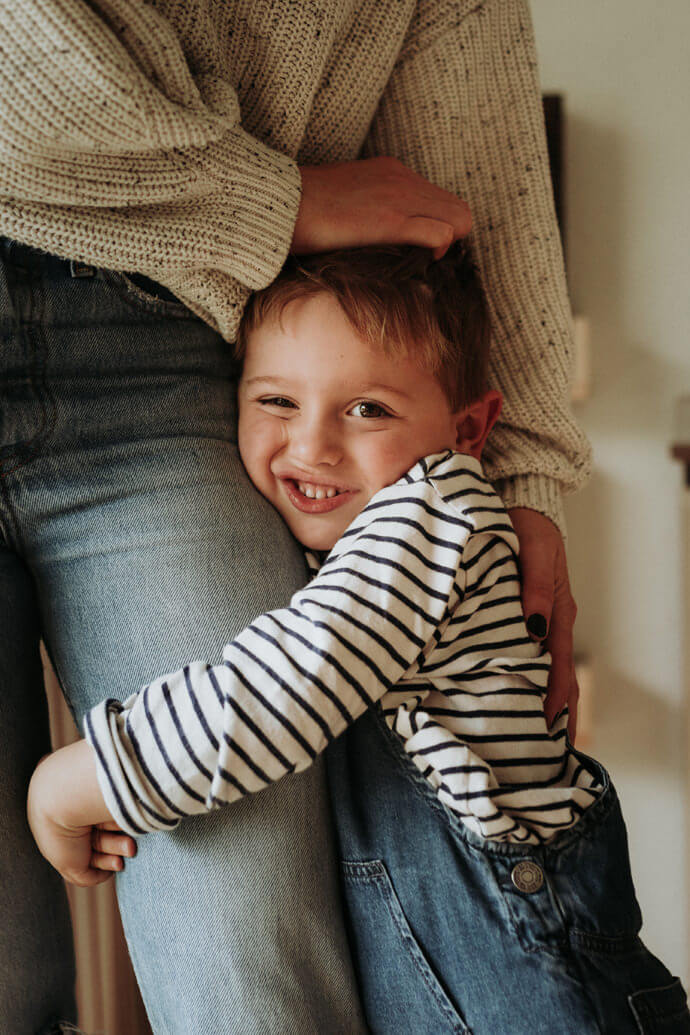 young boy smiling clinging to mums leg at family photoshoot southampton relaxed natural family photography winchester