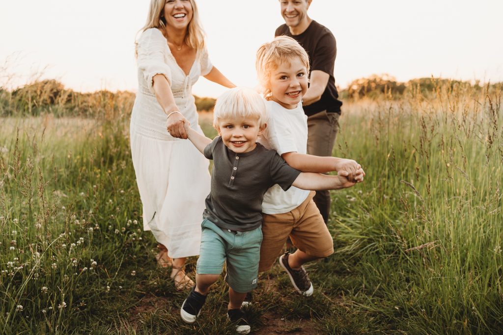2 boys pulling their parents through the long grass i a meadow on their photoshoot