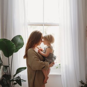 pregnant mama and her daughter balanced on her tummy standing in front of the window with sunlight streaming in