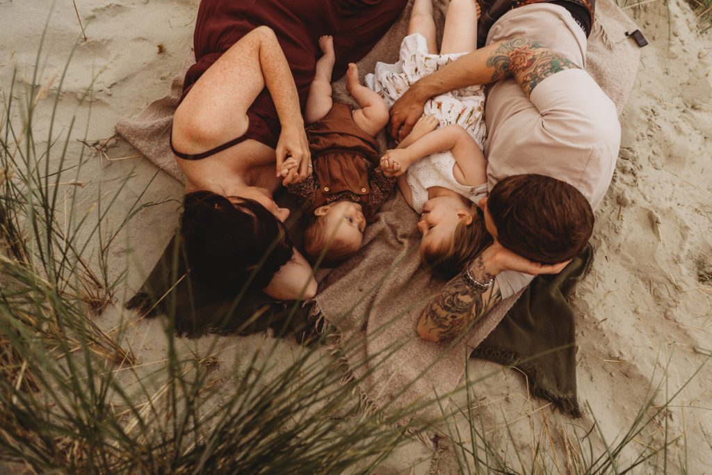 Family lying down cuddling on a blanket  in the sand dunes nestled between the grasses