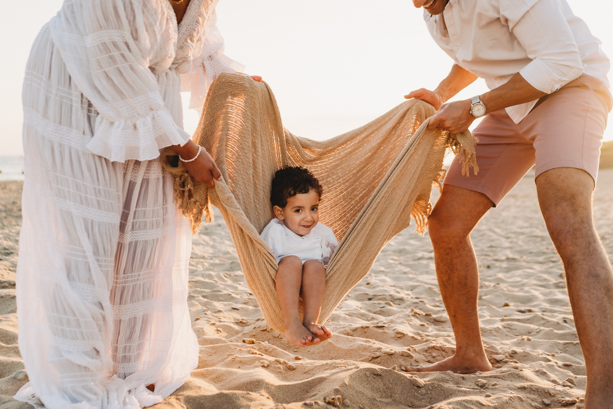 Baby swinging in blanket on the beach at sunset