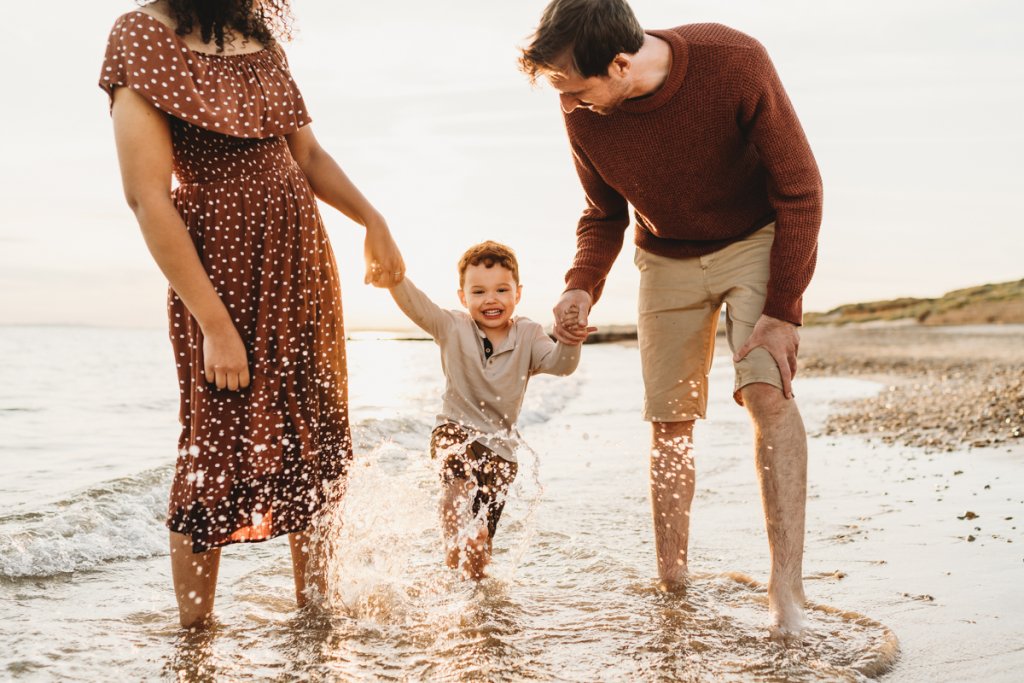 Family running and splashing in the sea hand in hand during a stunning sunset photoshoot
