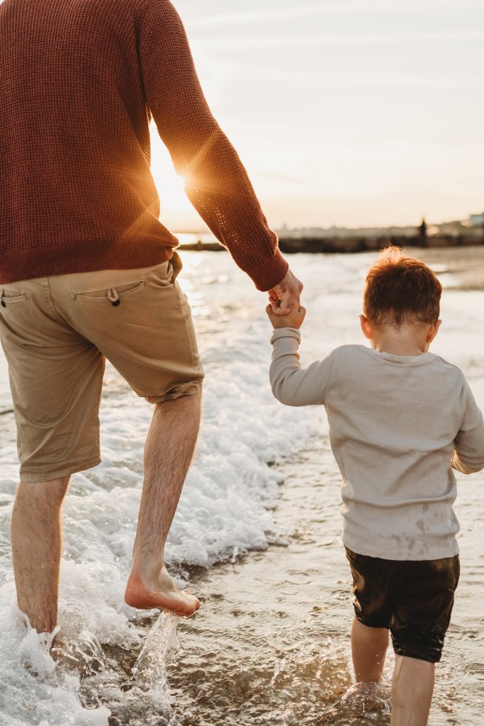 dad and son hold hand on beach during a family photography session  winchester 