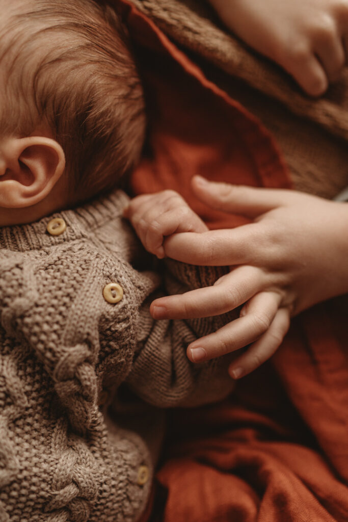 close up of baby holding brothers finger 