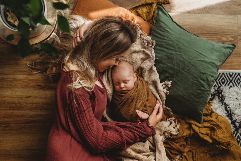 photo of mum lying on the floor at home smelling the head of her newborn baby 