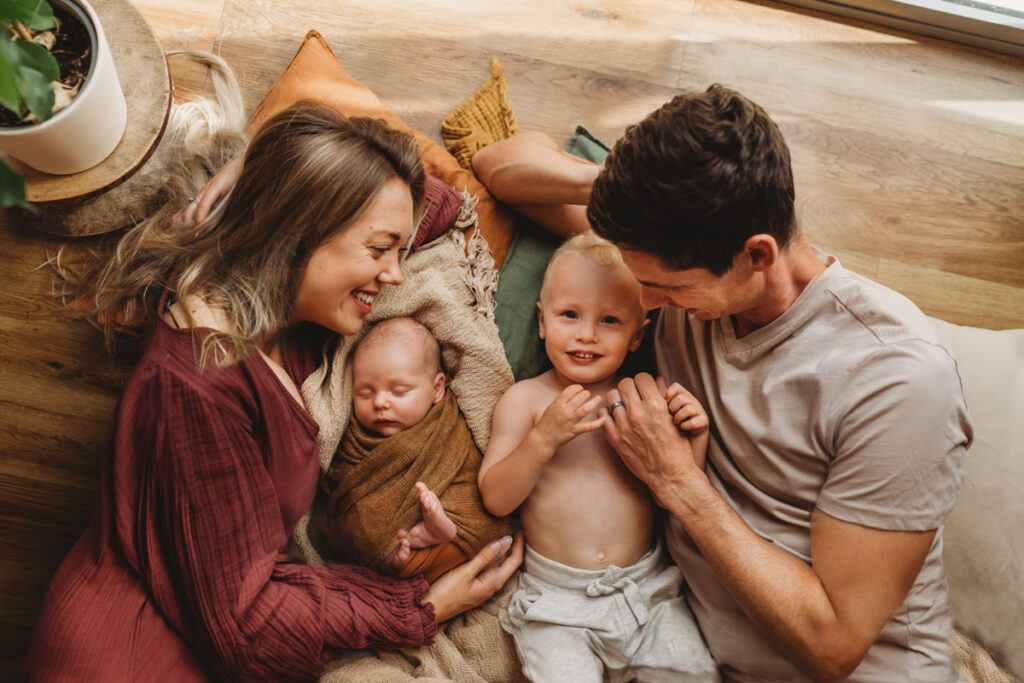 photo of family lying on the floor at home, little by smiles up at camera 